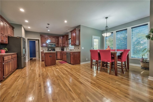 kitchen with appliances with stainless steel finishes, baseboards, a center island, and light wood finished floors