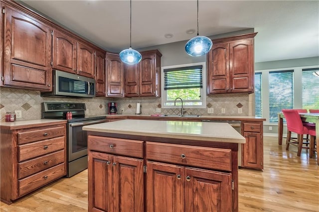 kitchen with a kitchen island, light countertops, a sink, light wood finished floors, and appliances with stainless steel finishes