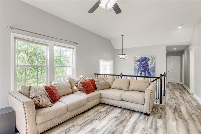 living area featuring vaulted ceiling, light wood finished floors, baseboards, and ceiling fan with notable chandelier
