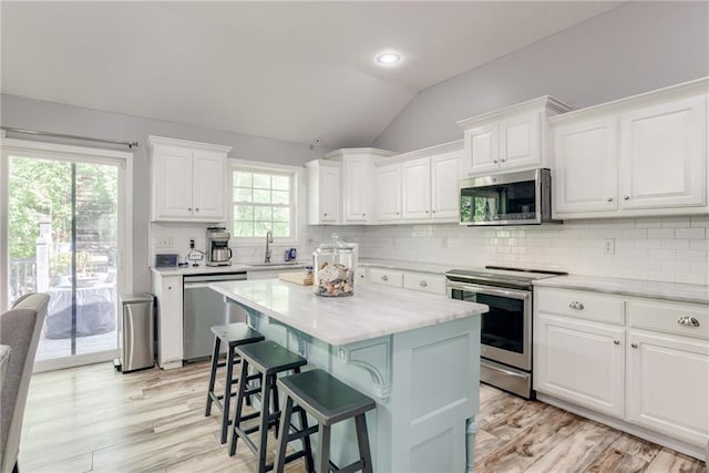 kitchen featuring a sink, a breakfast bar, white cabinets, lofted ceiling, and appliances with stainless steel finishes