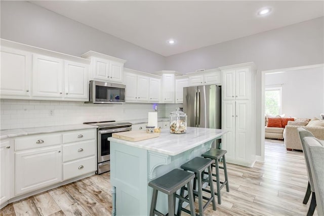 kitchen featuring white cabinets, appliances with stainless steel finishes, a kitchen breakfast bar, and light wood finished floors