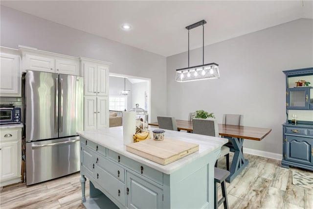 kitchen with white cabinets, a toaster, freestanding refrigerator, light wood-style floors, and a kitchen island