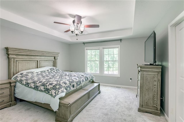 bedroom with light colored carpet, ceiling fan, baseboards, and a raised ceiling