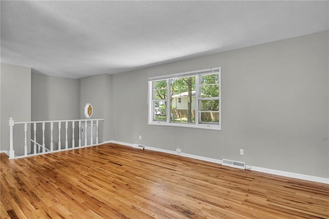 empty room with wood finished floors, a textured ceiling, and baseboards