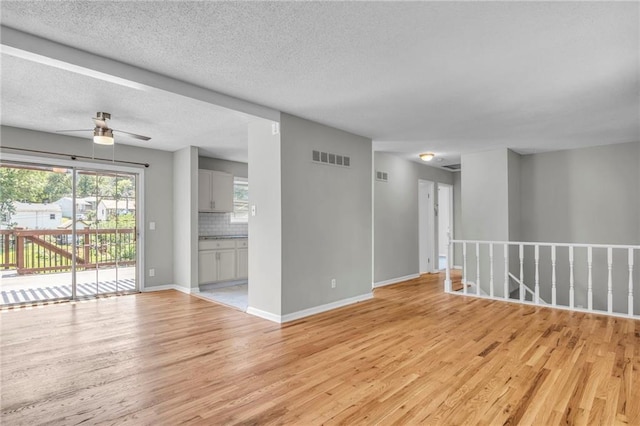 unfurnished living room with light wood-style flooring, ceiling fan, baseboards, and a textured ceiling