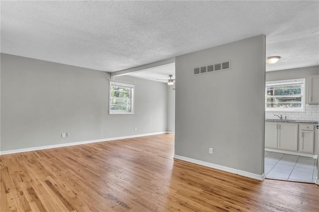 spare room with a textured ceiling, light wood-style floors, baseboards, and a sink