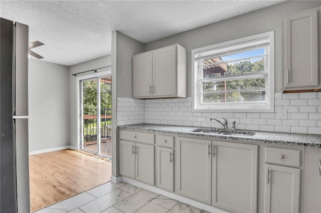 kitchen featuring a sink, decorative backsplash, a textured ceiling, and light stone counters