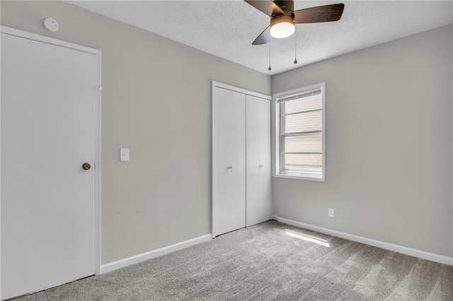 unfurnished bedroom with carpet flooring, a closet, baseboards, a textured ceiling, and a ceiling fan