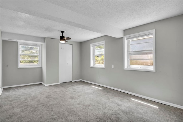 unfurnished bedroom with a textured ceiling, multiple windows, carpet, and baseboards