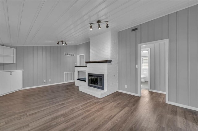 unfurnished living room featuring a brick fireplace, wood finished floors, and visible vents