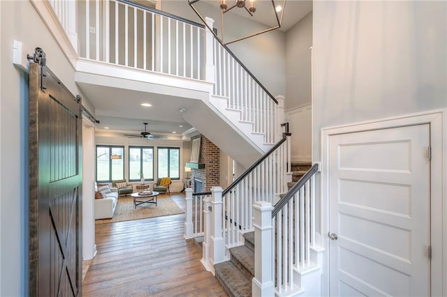 8120 Lone Elm Rd, Lenexa, KS 66220 - stairway featuring a barn door, a towering ceiling, wood finished floors, ceiling fan, and a fireplace