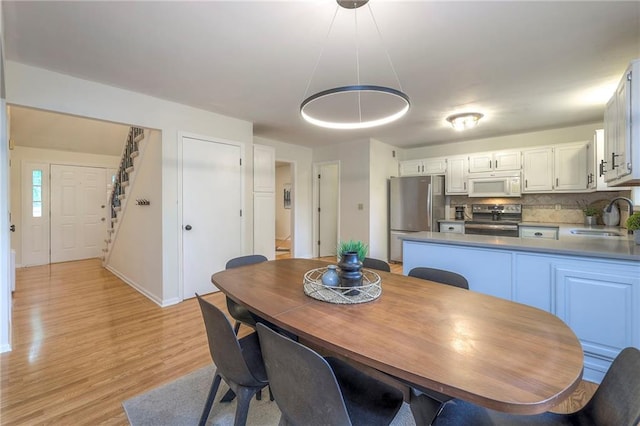 dining area with stairs, light wood-style flooring, and baseboards