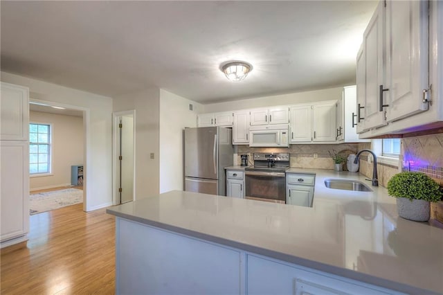 kitchen with appliances with stainless steel finishes, a sink, backsplash, light wood-style floors, and a peninsula