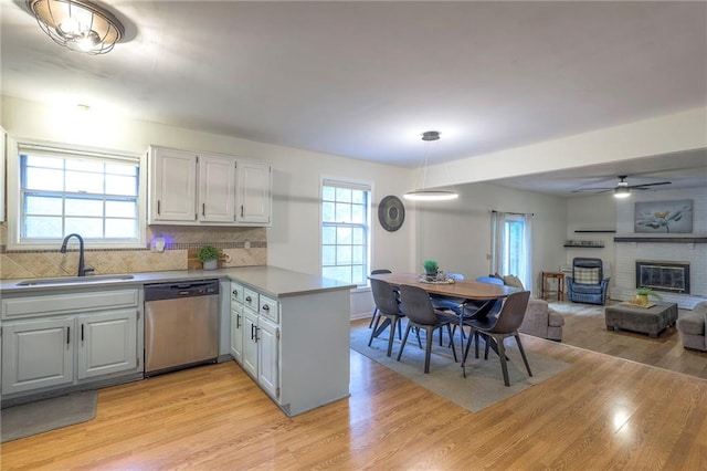 kitchen with dishwasher, a peninsula, a sink, a fireplace, and light wood-style flooring