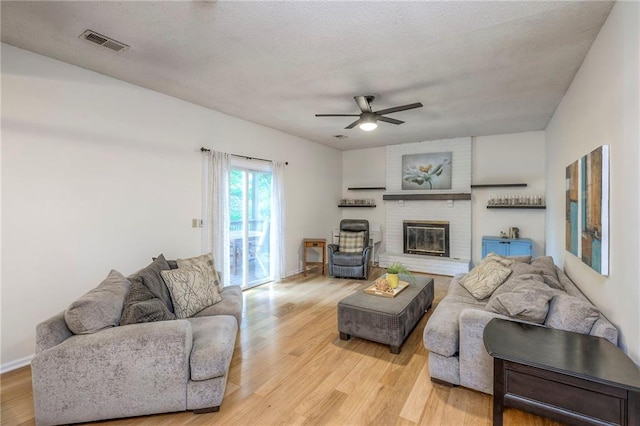 living area featuring light wood-type flooring, ceiling fan, a brick fireplace, a textured ceiling, and baseboards