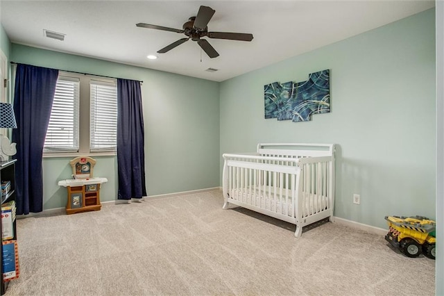 bedroom with carpet flooring, a crib, a ceiling fan, baseboards, and visible vents
