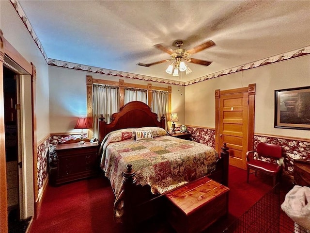 bedroom with wainscoting, dark carpet, ceiling fan, and a textured ceiling