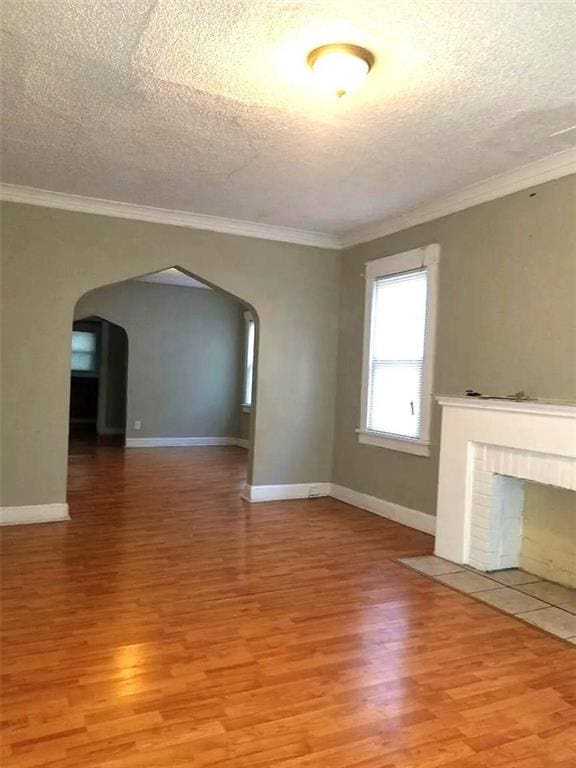 2109 E 58th St, Kansas City, MO 64130 - unfurnished living room featuring arched walkways, light wood-type flooring, a textured ceiling, crown molding, and a fireplace