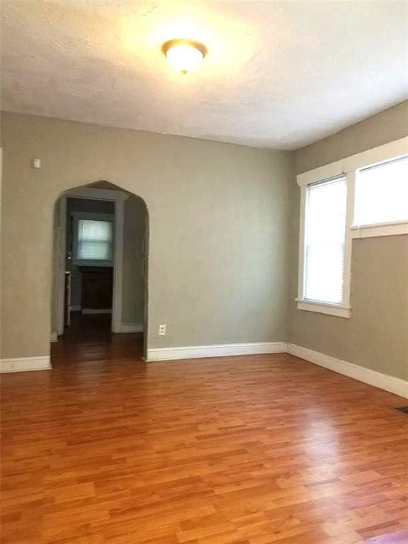 2109 E 58th St, Kansas City, MO 64130 - empty room with arched walkways, light wood finished floors, and baseboards