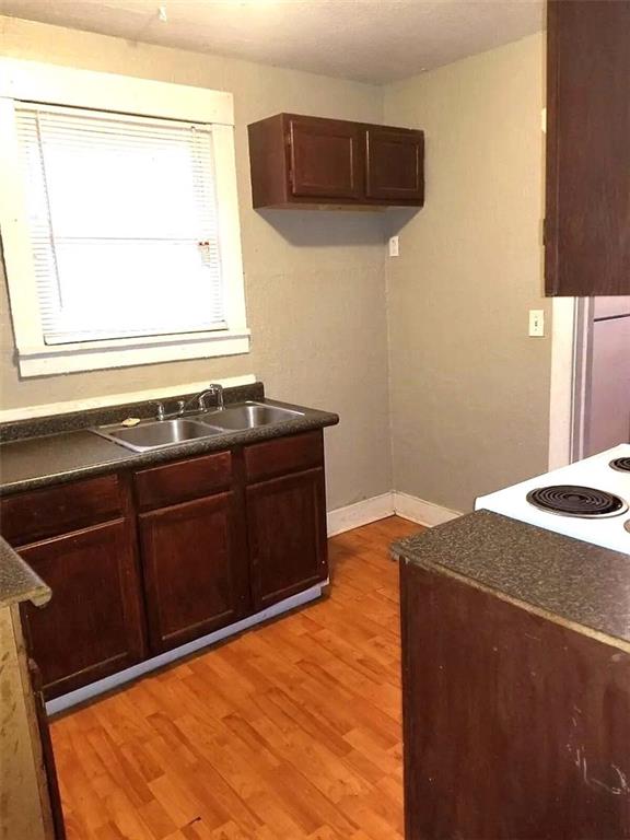 2109 E 58th St, Kansas City, MO 64130 - kitchen featuring dark countertops, a sink, light wood-type flooring, baseboards, and dark brown cabinetry