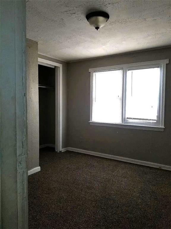 2109 E 58th St, Kansas City, MO 64130 - unfurnished bedroom featuring a closet, a textured ceiling, baseboards, and dark colored carpet