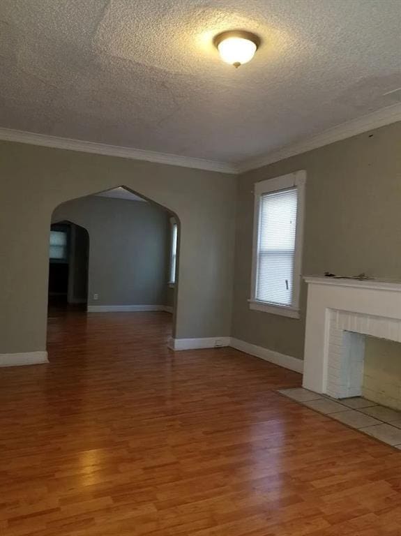2109 E 58th St, Kansas City, MO 64130 - unfurnished living room featuring arched walkways, light wood finished floors, a textured ceiling, crown molding, and baseboards