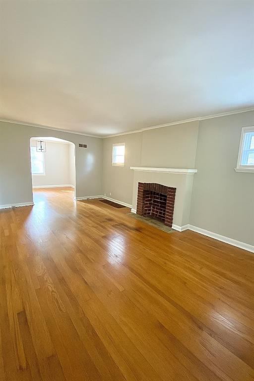 5610 Euclid Ave, Kansas City, MO 64130 - unfurnished living room with wood finished floors, a fireplace, ornamental molding, and arched walkways