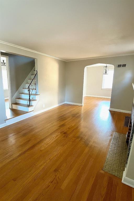 5610 Euclid Ave, Kansas City, MO 64130 - unfurnished living room featuring wood finished floors, stairs, crown molding, and arched walkways