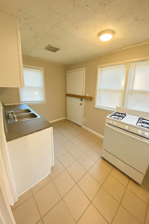 5610 Euclid Ave, Kansas City, MO 64130 - kitchen featuring white gas range oven, light tile patterned floors, white cabinetry, and a textured ceiling