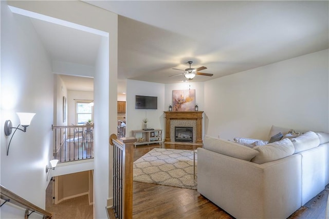 living room featuring a ceiling fan, baseboards, a tiled fireplace, and wood finished floors
