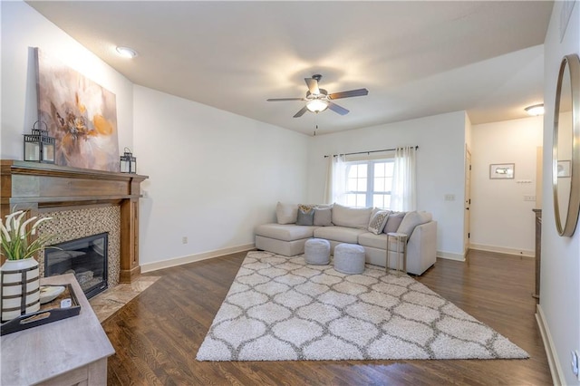 living area featuring baseboards, a ceiling fan, dark wood finished floors, and a tiled fireplace