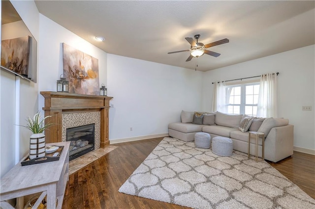 living area featuring baseboards, ceiling fan, a tiled fireplace, and wood finished floors