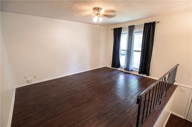 empty room with dark wood-style flooring, a ceiling fan, a textured ceiling, and baseboards