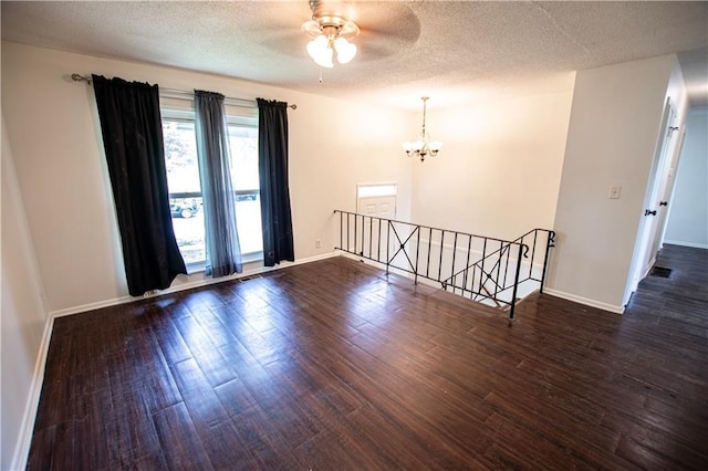 empty room featuring a chandelier, dark wood-type flooring, baseboards, a ceiling fan, and a textured ceiling