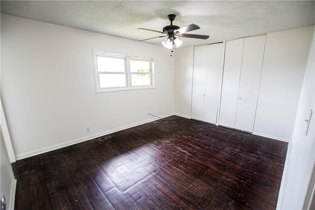 unfurnished bedroom featuring two closets, dark wood-style floors, a textured ceiling, a ceiling fan, and baseboards
