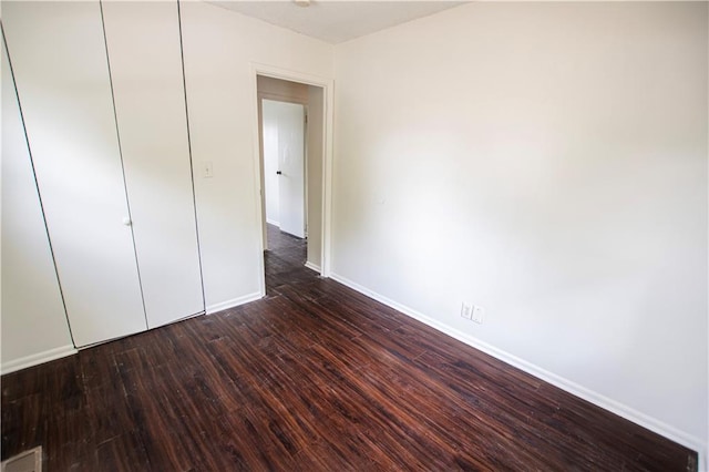 unfurnished bedroom featuring baseboards, dark wood-style flooring, and a closet