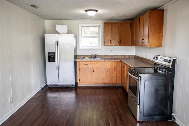 kitchen with appliances with stainless steel finishes, a sink, dark wood finished floors, brown cabinetry, and a textured ceiling