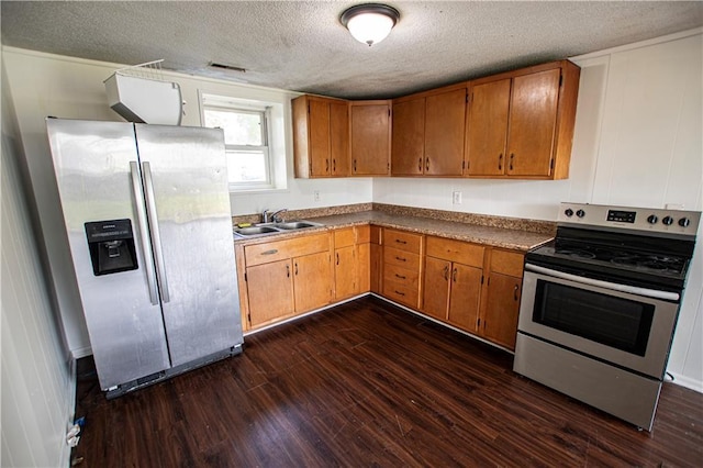 kitchen with stainless steel appliances, dark wood-type flooring, a textured ceiling, brown cabinetry, and a sink
