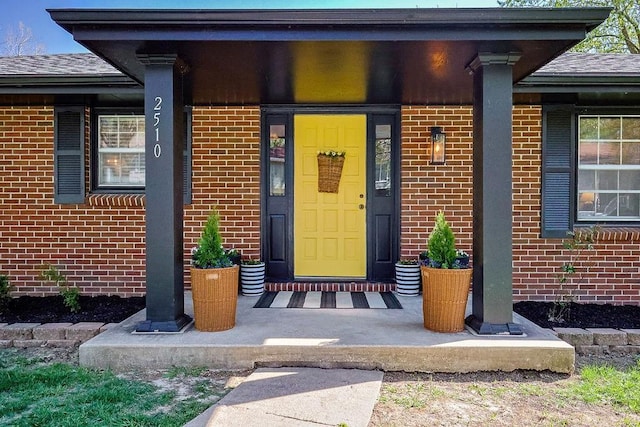 view of exterior entry featuring brick siding, a shingled roof, and covered porch