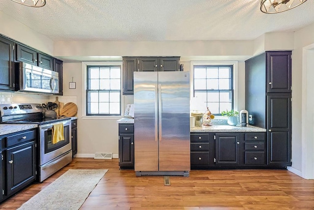 kitchen featuring stainless steel appliances, light wood-type flooring, a textured ceiling, and baseboards