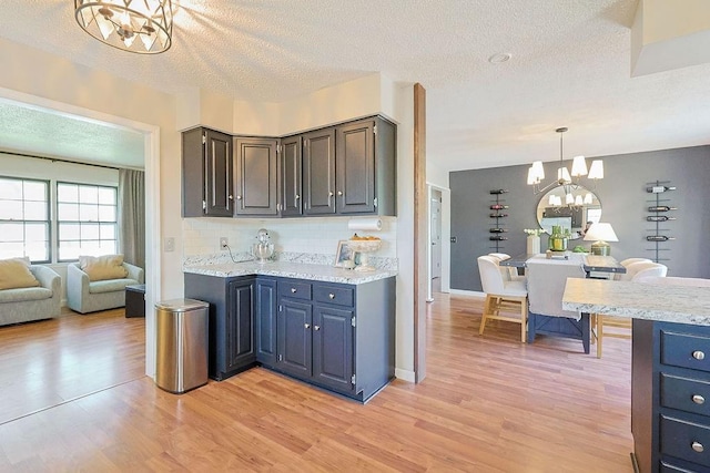 kitchen featuring a chandelier, light wood-style flooring, a textured ceiling, tasteful backsplash, and decorative light fixtures