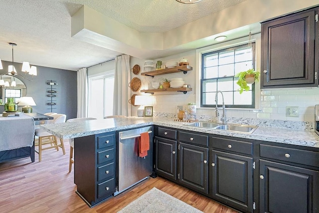 kitchen featuring dishwasher, a textured ceiling, a sink, decorative backsplash, and a chandelier