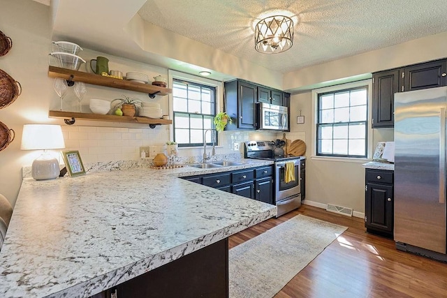 kitchen featuring stainless steel appliances, a sink, healthy amount of natural light, tasteful backsplash, and a textured ceiling