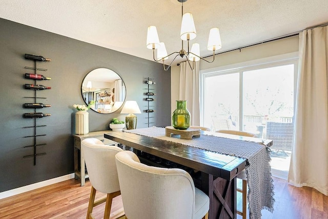 dining area featuring a chandelier, light wood-style flooring, a textured ceiling, and baseboards