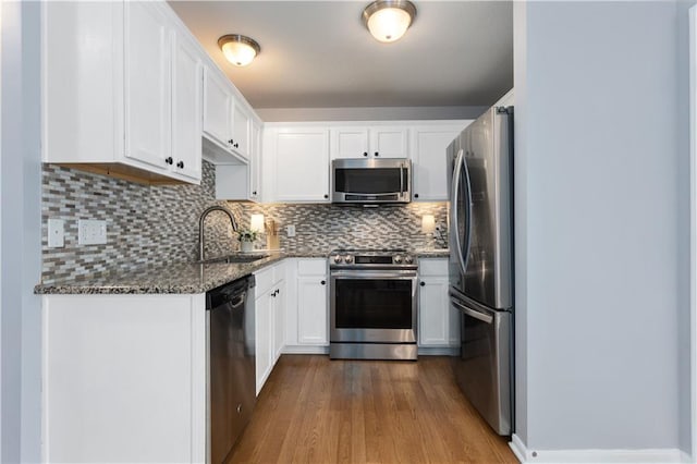 kitchen with dark stone counters, a sink, appliances with stainless steel finishes, white cabinetry, and dark wood-style floors