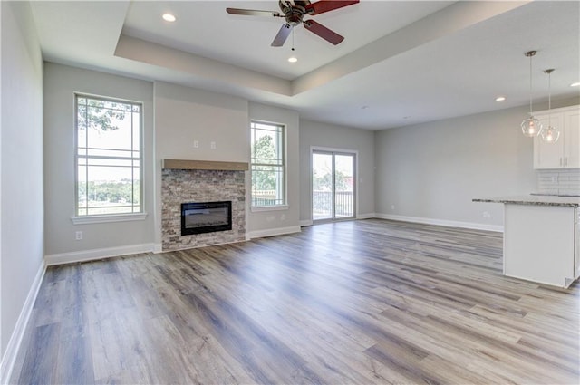 1828 N 92nd Ter, Kansas City, KS 66112 - unfurnished living room featuring light wood finished floors, a tray ceiling, baseboards, ceiling fan, and a fireplace