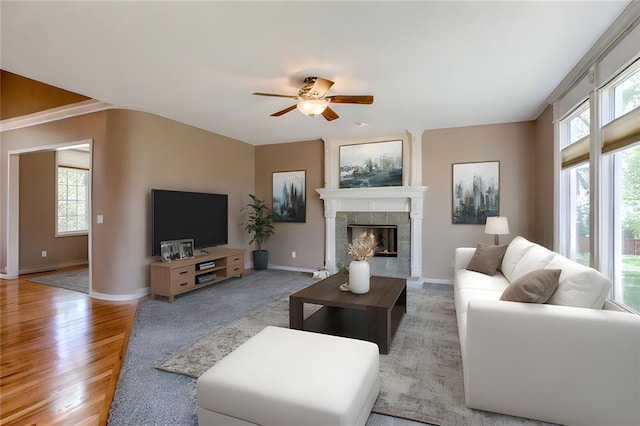 living area with a fireplace, wood finished floors, a ceiling fan, and baseboards