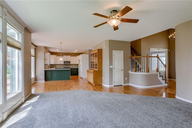 unfurnished living room with light carpet, baseboards, stairs, and a healthy amount of sunlight
