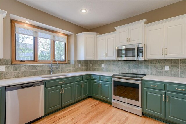 kitchen with a sink, light countertops, appliances with stainless steel finishes, white cabinetry, and green cabinetry