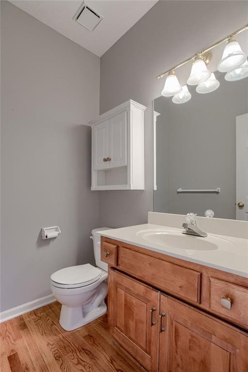 bathroom with wood finished floors, vanity, baseboards, toilet, and visible vents
